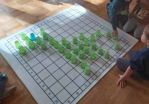 Dzieci układają na macie do kodowania kolorowe kubki